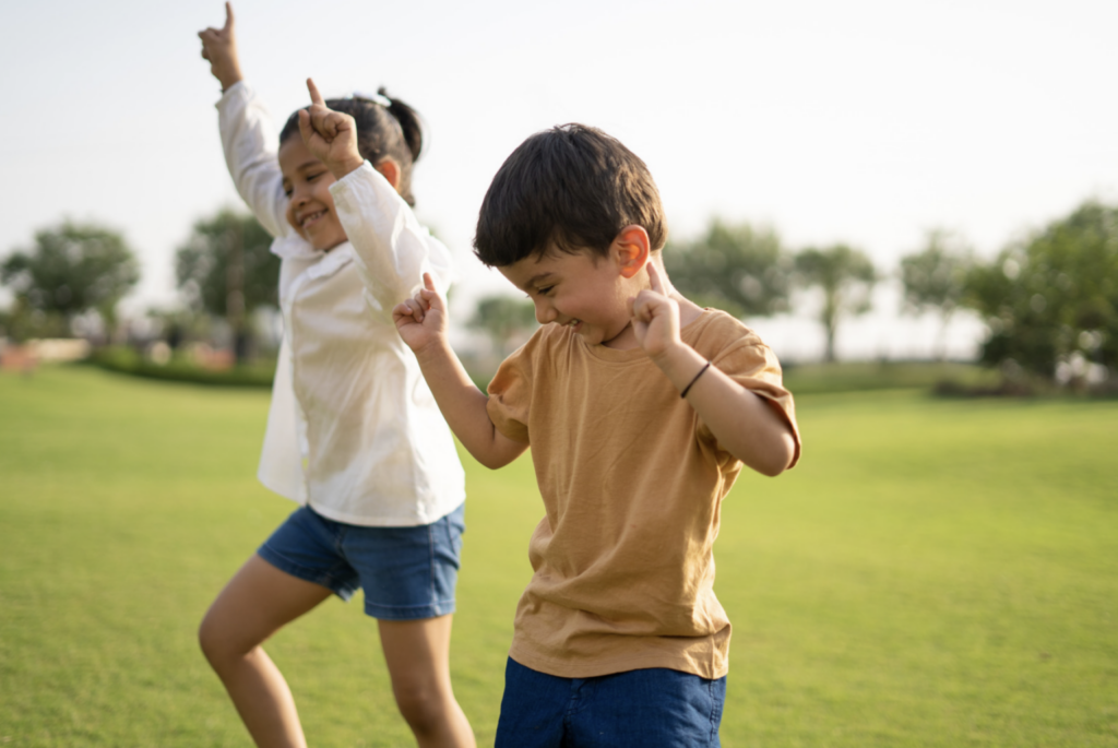 Brother and Sister laughing and dancing in the park on a sunny day.